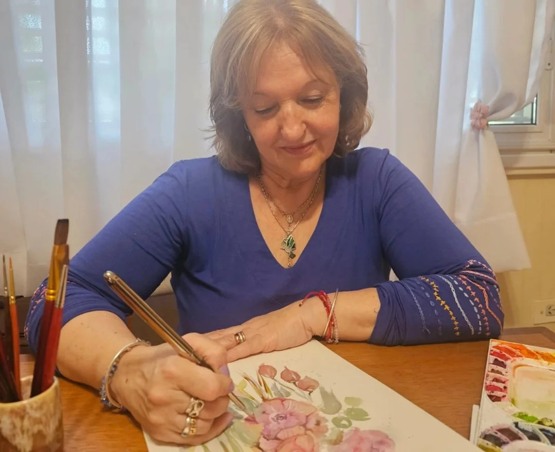 Liliana Donato pintando una acuarela de flores, con los pinceles y la paleta sobre la mesa.