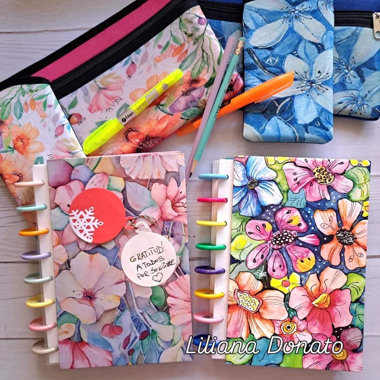Cartucheras y cuadernos anillados con estampas de flores en acuarela, en rosas, naranjas y azules.