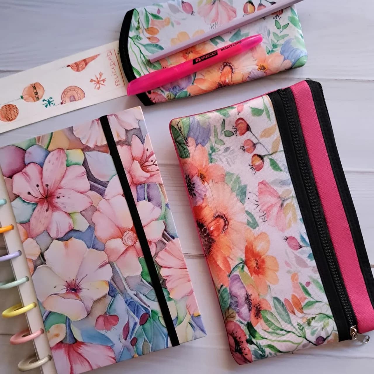 Cuaderno de tapa dura, estuche y cartuchera con una acuarela de flores en tonos rosas y durazno.